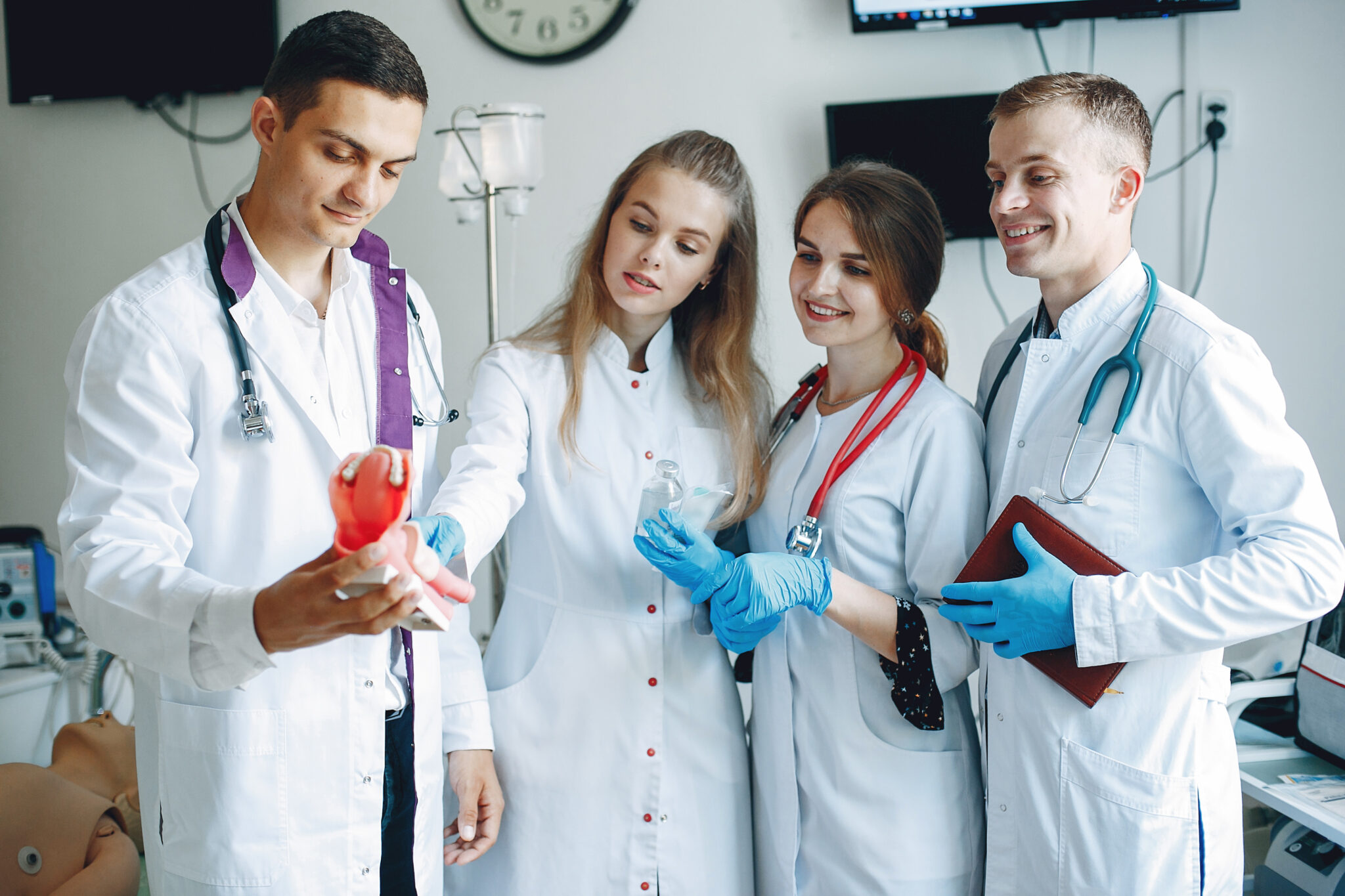Men and women in hospital gowns hold medical equipment in their hands. Students practice medicine.